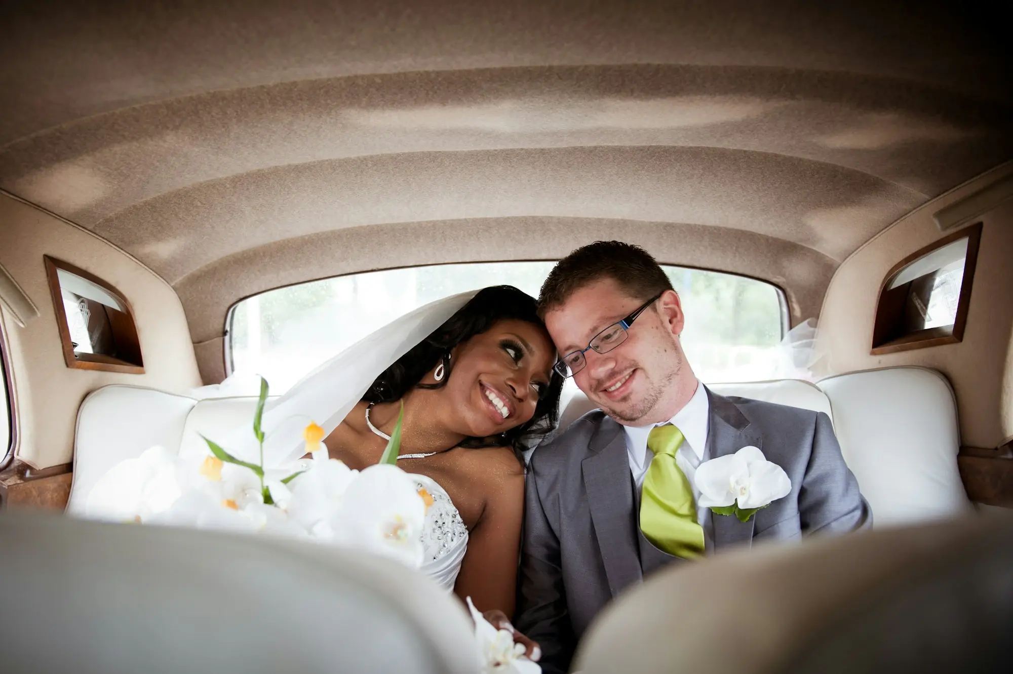 A newly married couple laughing together in the back of a limousine