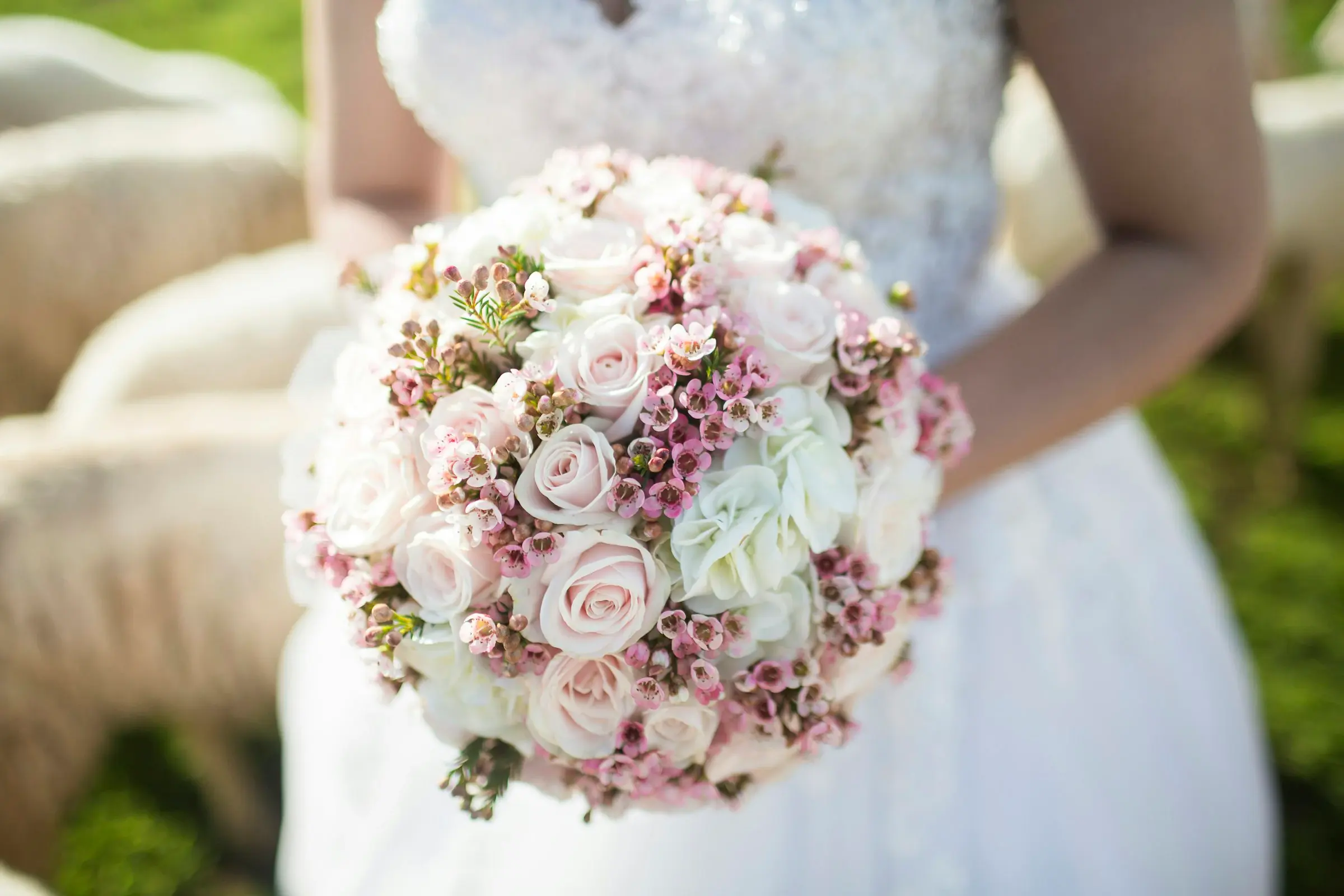 A bride holding a bouquet of pink and cream roses against her gown