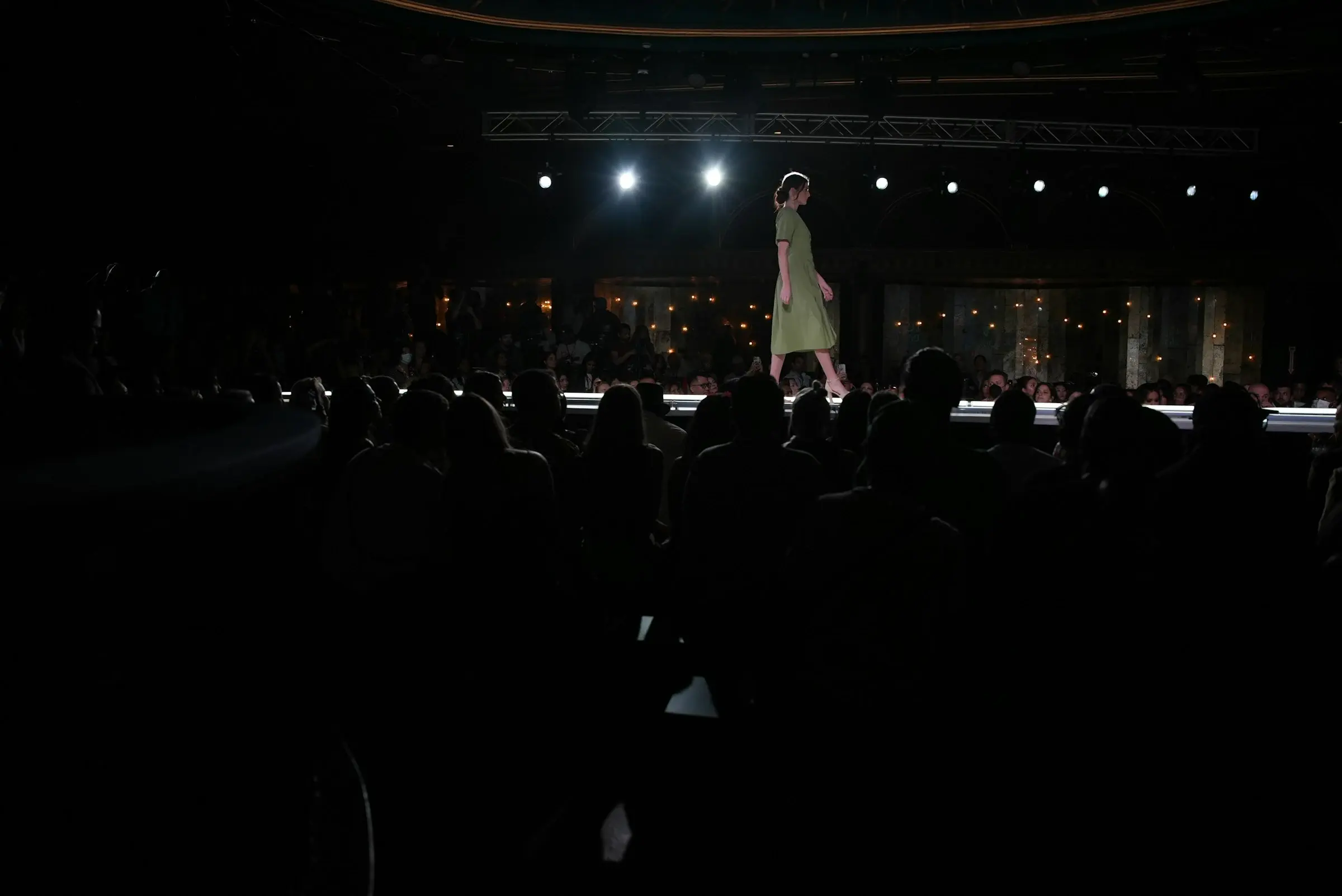 A model on a long runway in a darkened hall, the audience seated on both sides